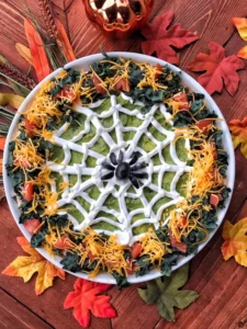 A spider made of olives in the middle of a spooky dip with sour cream webbing.