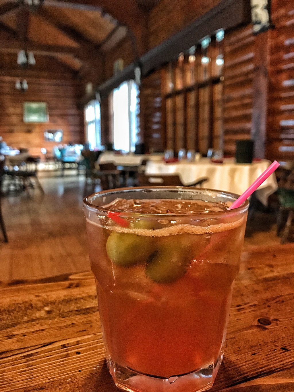 A brandy Old Fashioned in a glass with a pink straw in a rustic lodge style restaurant.