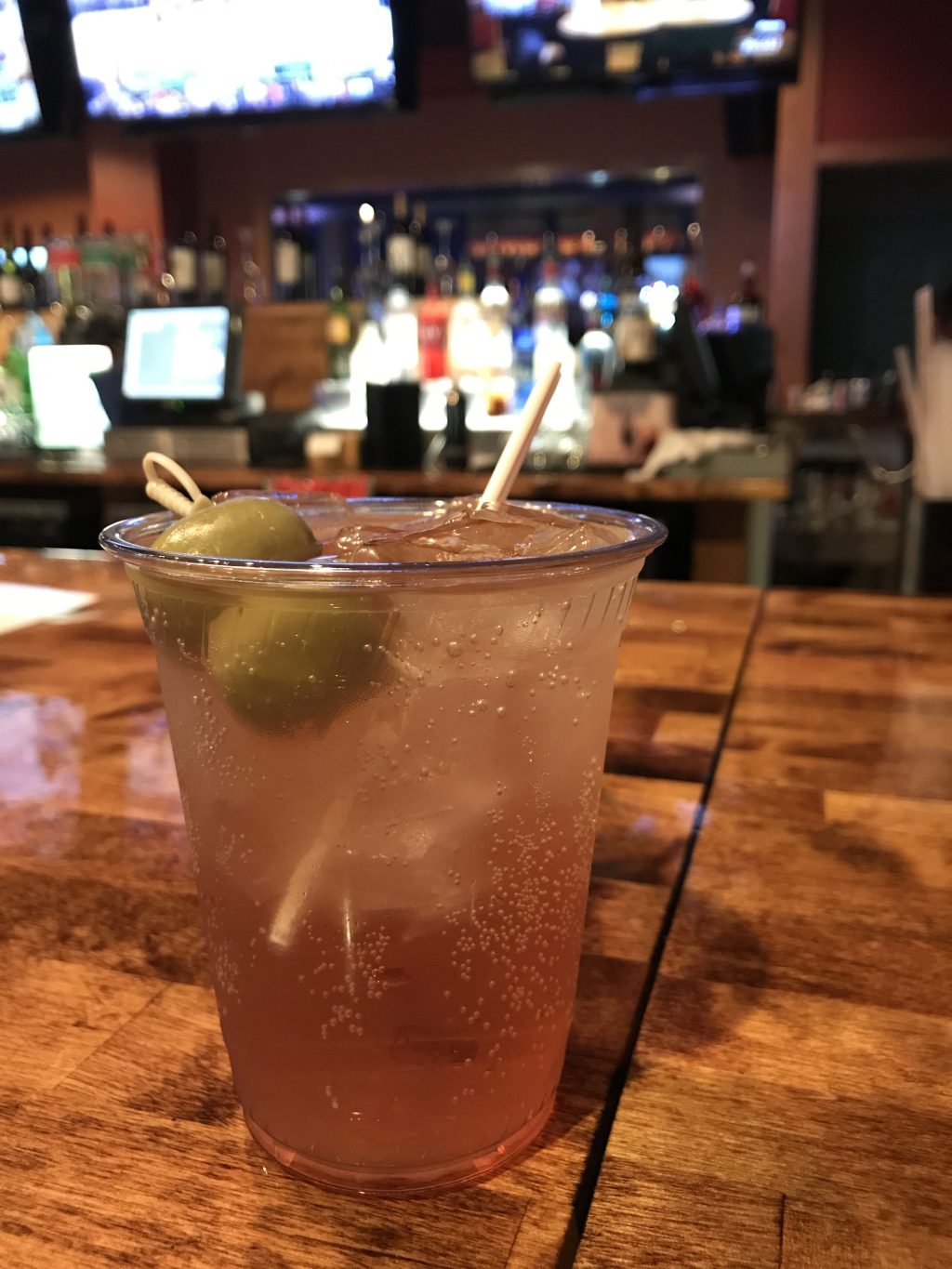 A brandy Old Fashioned in a plastic cup on a bar.