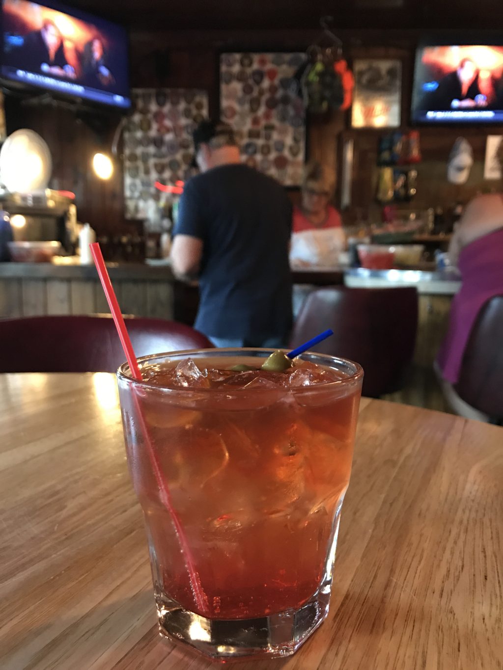 A brandy Old Fashioned on a table with a person in a black shirt in the background facing away.