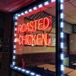 A neon sign in a window that reads "Roasted Chicken."