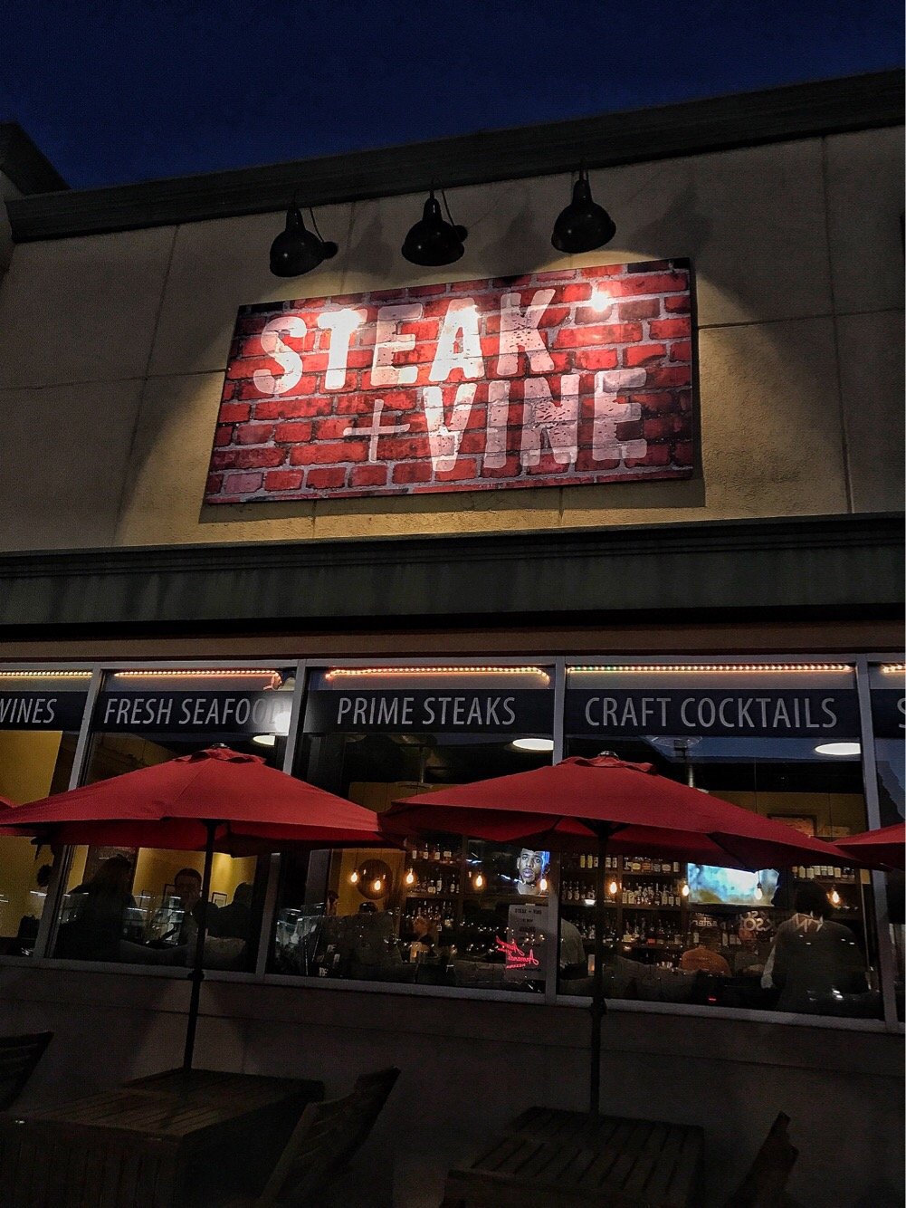 The exterior of the Steak + Vine restaurant. Signs in the windows read "Fresh Seafood, Prime Steaks, and Craft Cocktails."