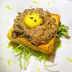 Beef tartare on square toast with a quail egg on top.