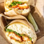 A pork katsu sandwich in a box with a pickle.