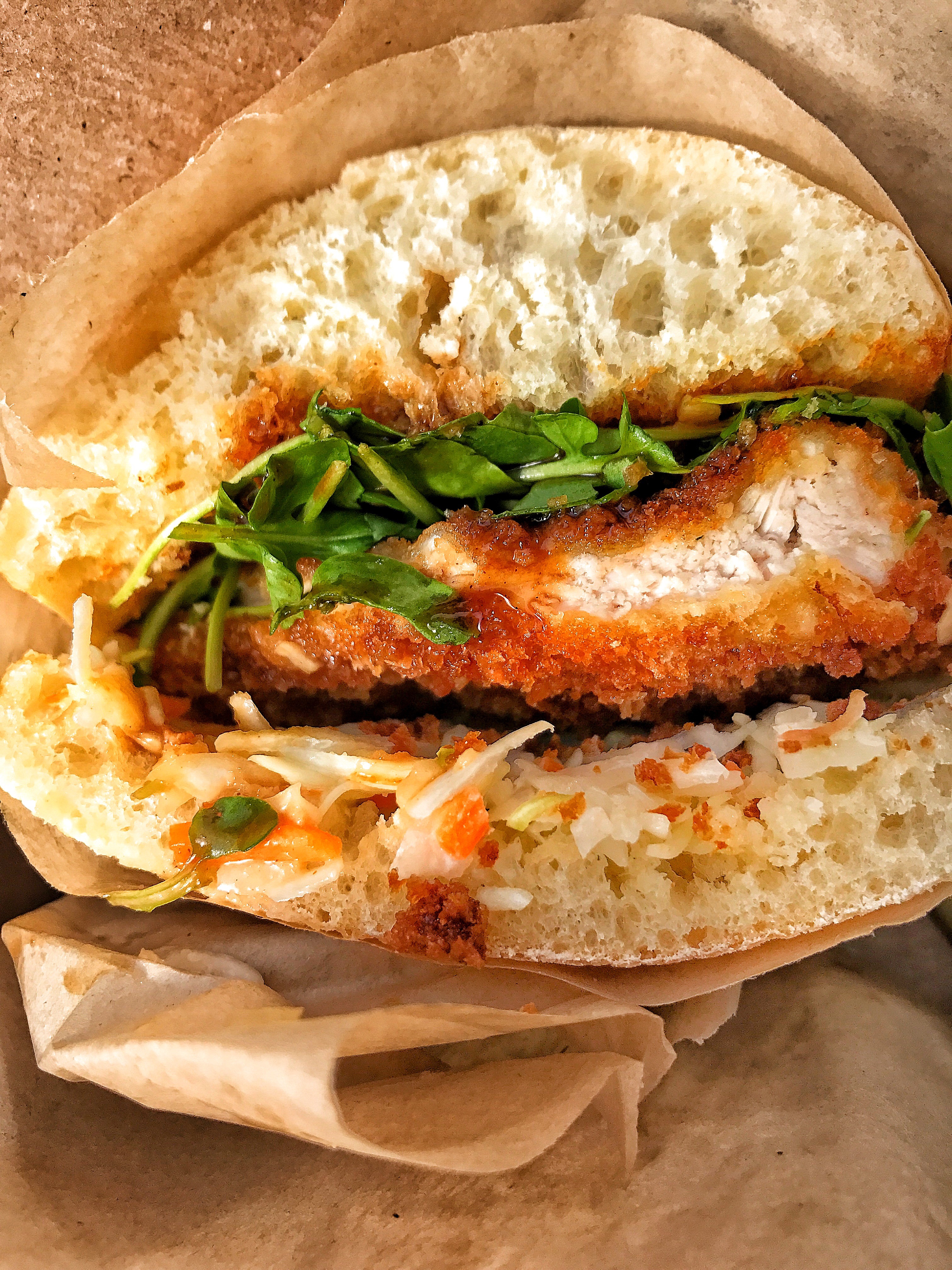 A close up of a fried pork cutlet sandwich with greens and slaw.