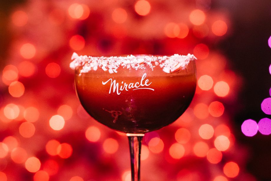 A cocktail glass with the word "miracle" written on it in front of a red background.