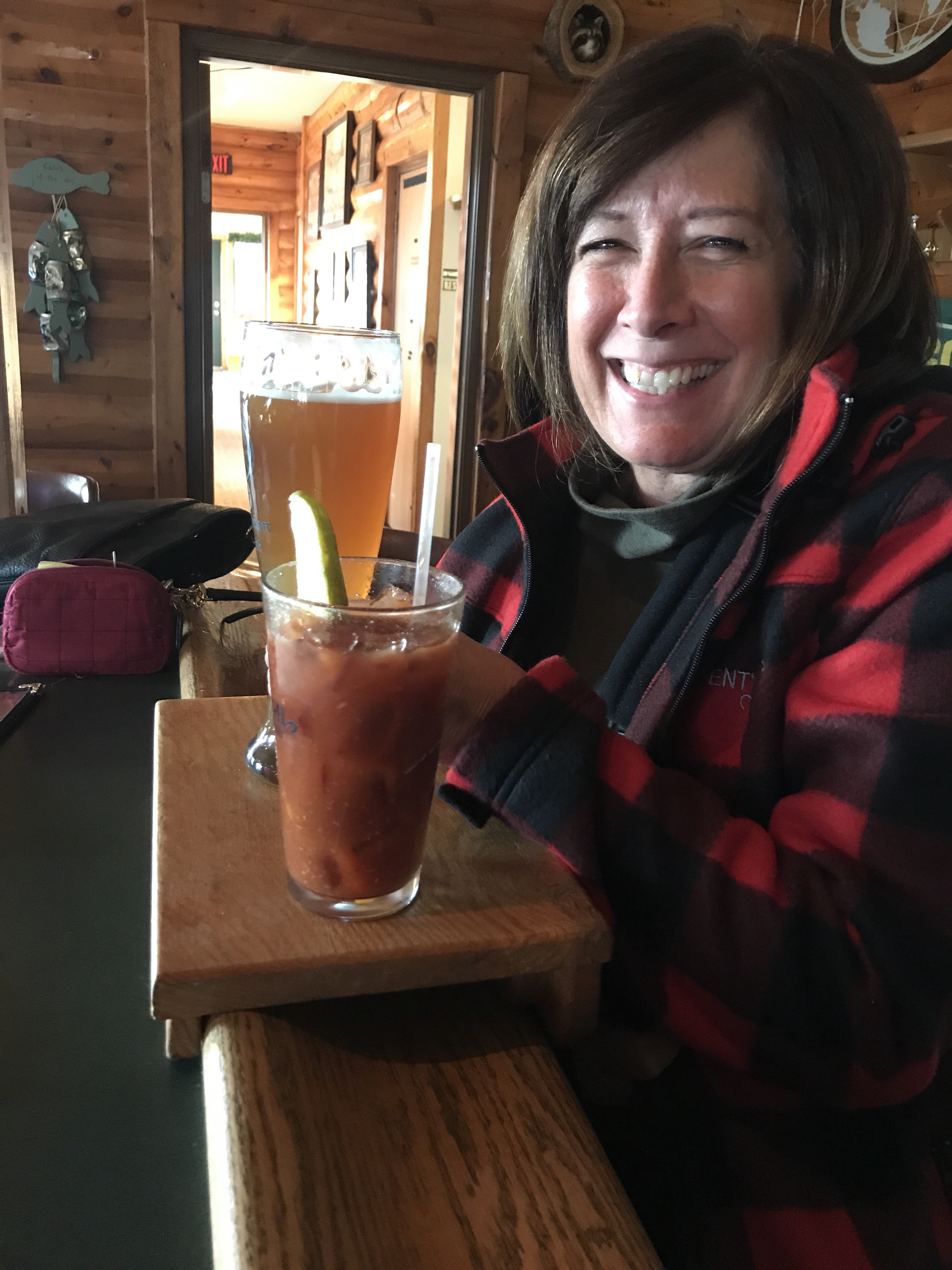 My mom sitting at a bar with a Bloody Mary and a beer on a wooden tray.
