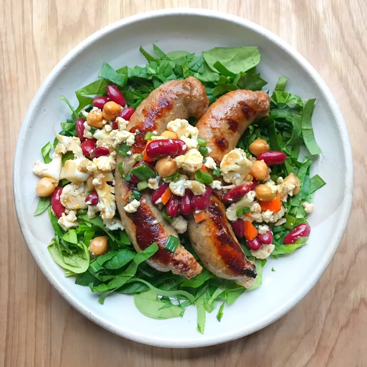 Sausages over a green salad topped with bean and cauliflower giardiniera.