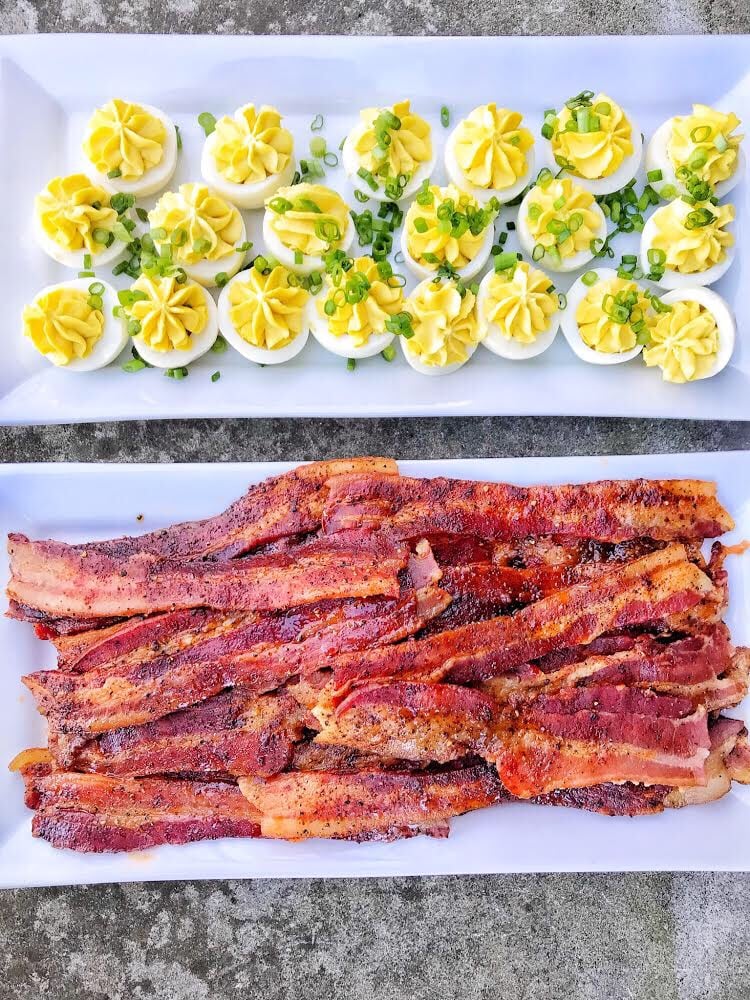 A rectangular plate of deviled eggs next to a rectangular plate of candied bacon.