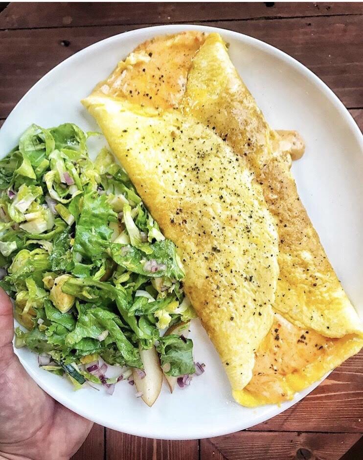 An egg omelette topped with pepper on a plate next to a green salad.