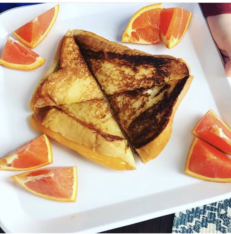 A grilled cheese sandwich sliced into four pieces with orange wedges.