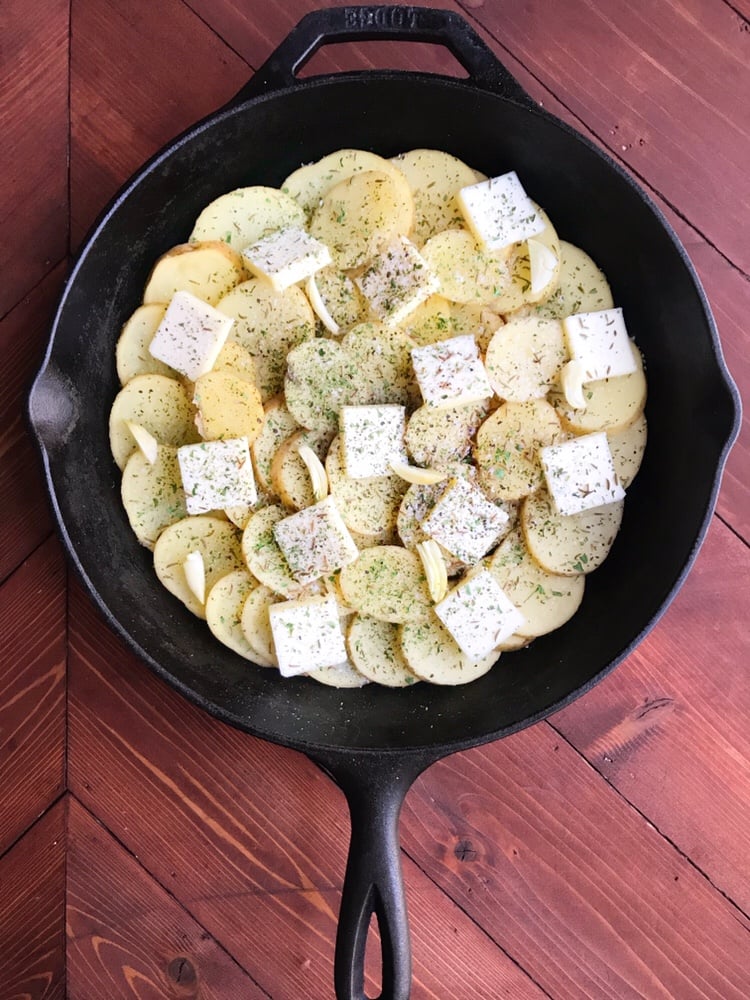 Sliced potatoes, butter, and garlic in a cast iron skillet seen from above.