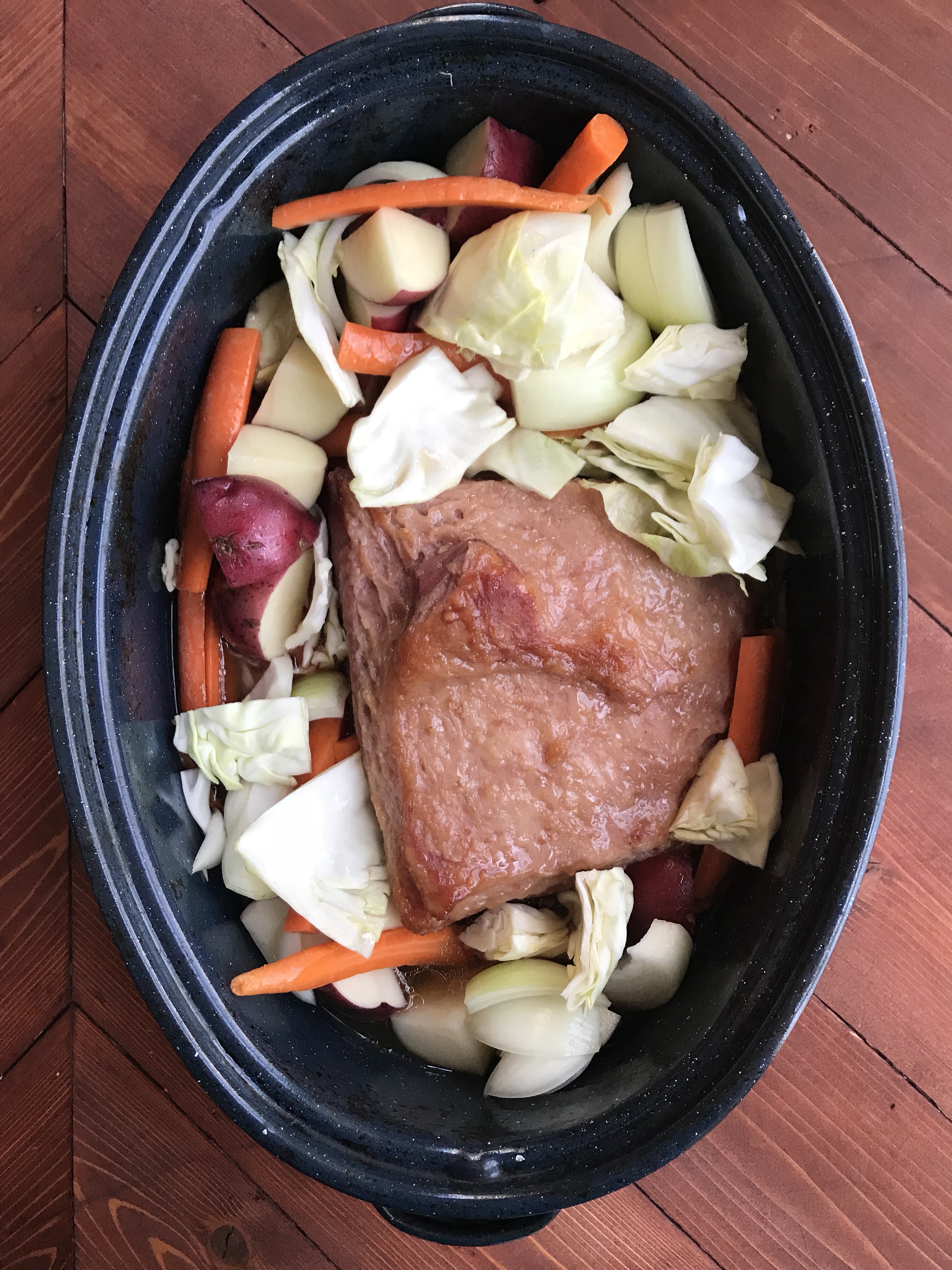Corned beef in a roasting dish with cabbage, potatoes, and carrots.