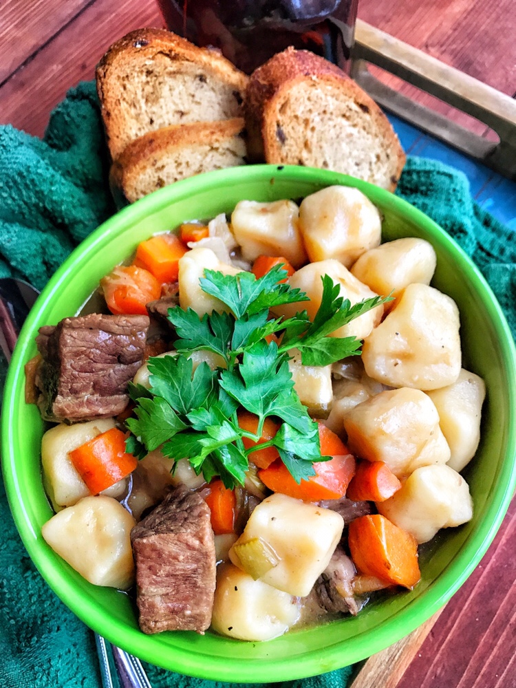 Irish Stew with potato dumplings in a green bowl with slices of bread by the side.