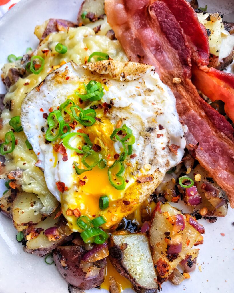 A fried egg topped with chopped green onion over breakfast potatoes and bacon.