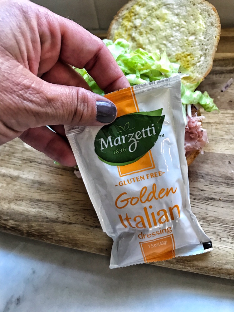 A packet of Golden Italian dressing held in front of a ham sandwich.