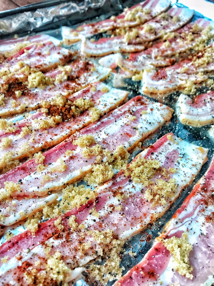 A close up view of raw bacon slices covered in pepper, brown sugar, and chili powder.
