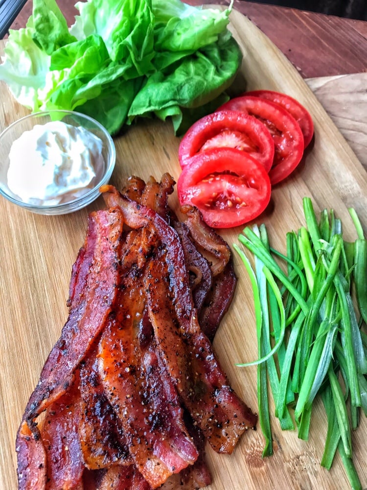The cooked bacon on a cutting board next to mayo, sliced tomatoes, lettuce, and sliced scallions.