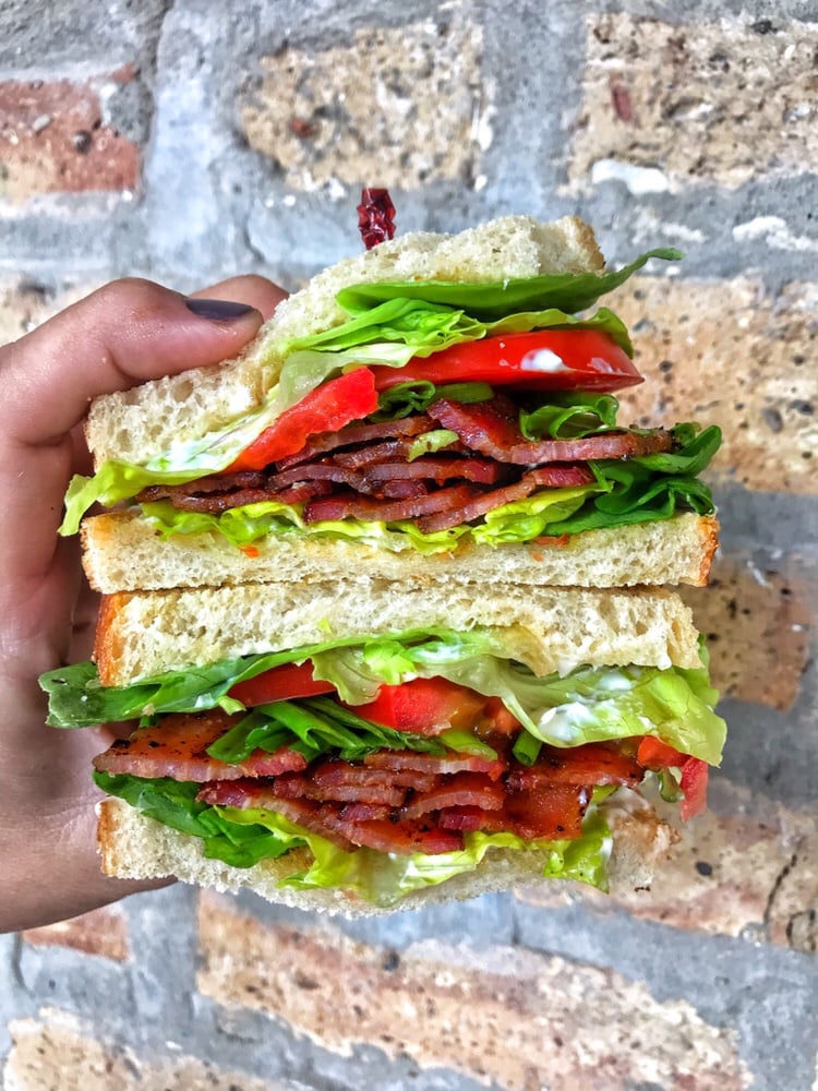 Two halves of a finished BLT being held in one hand, one above the other.