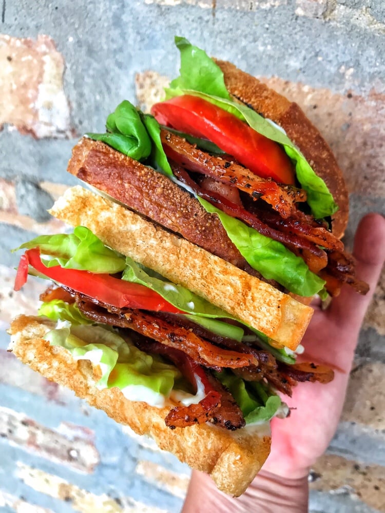 Another angle of two halves of a finished BLT being held in one hand, one above the other.