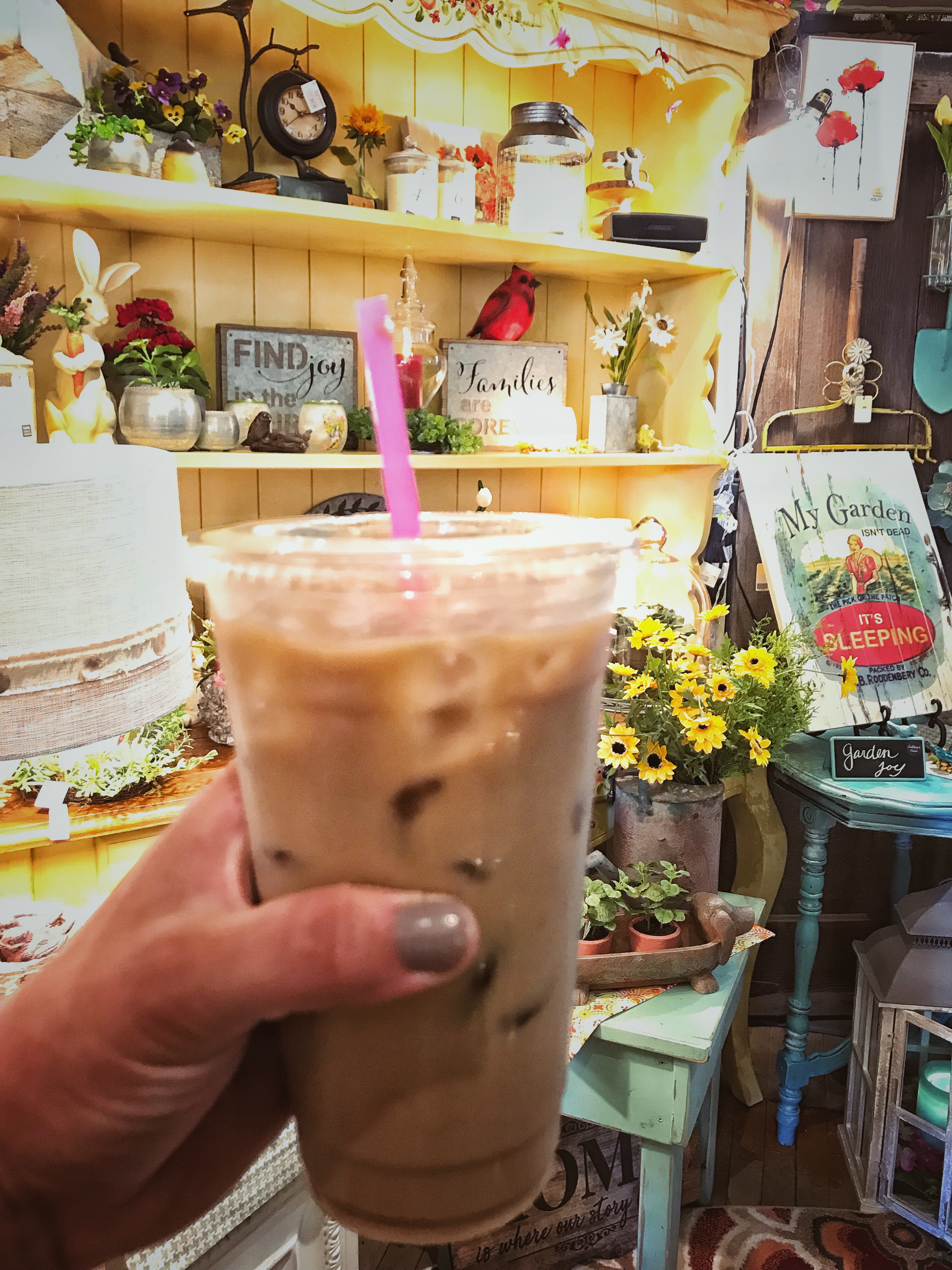 An iced coffee with a pink straw being held inside of Tricia's Treasures.