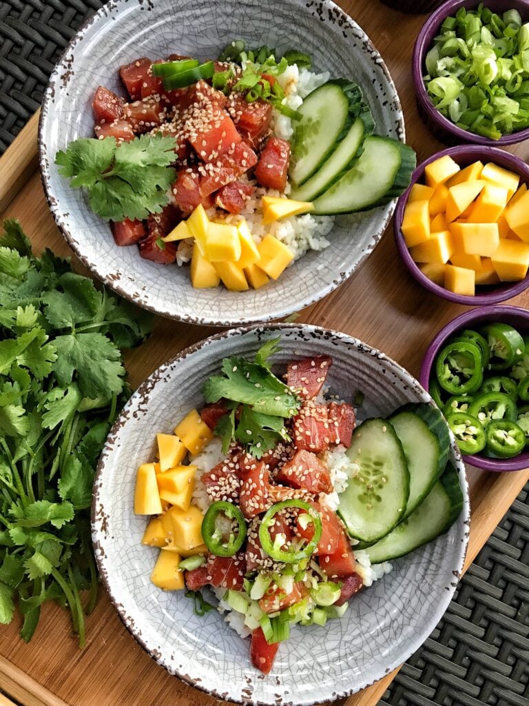 Two rice bowls with cubes of tuna, mango, cucumber slices, and sesame seeds.