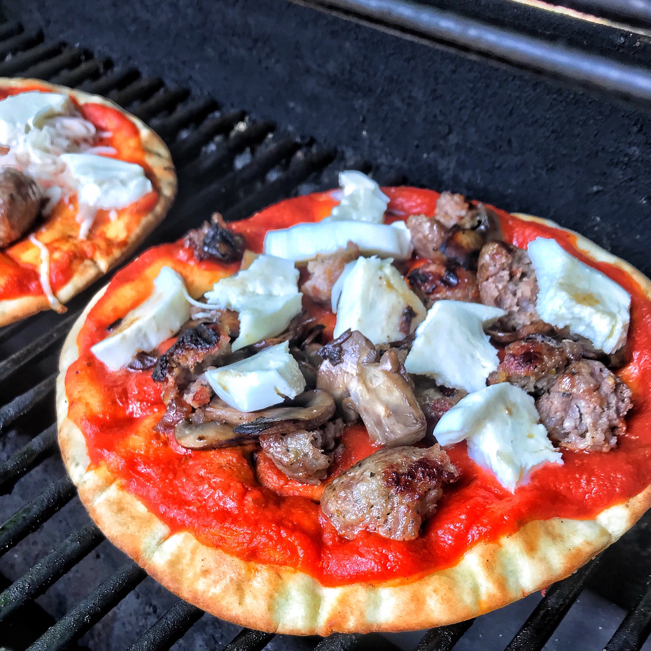 Pizza on the grill topped with cheese, mushrooms, and sausage.