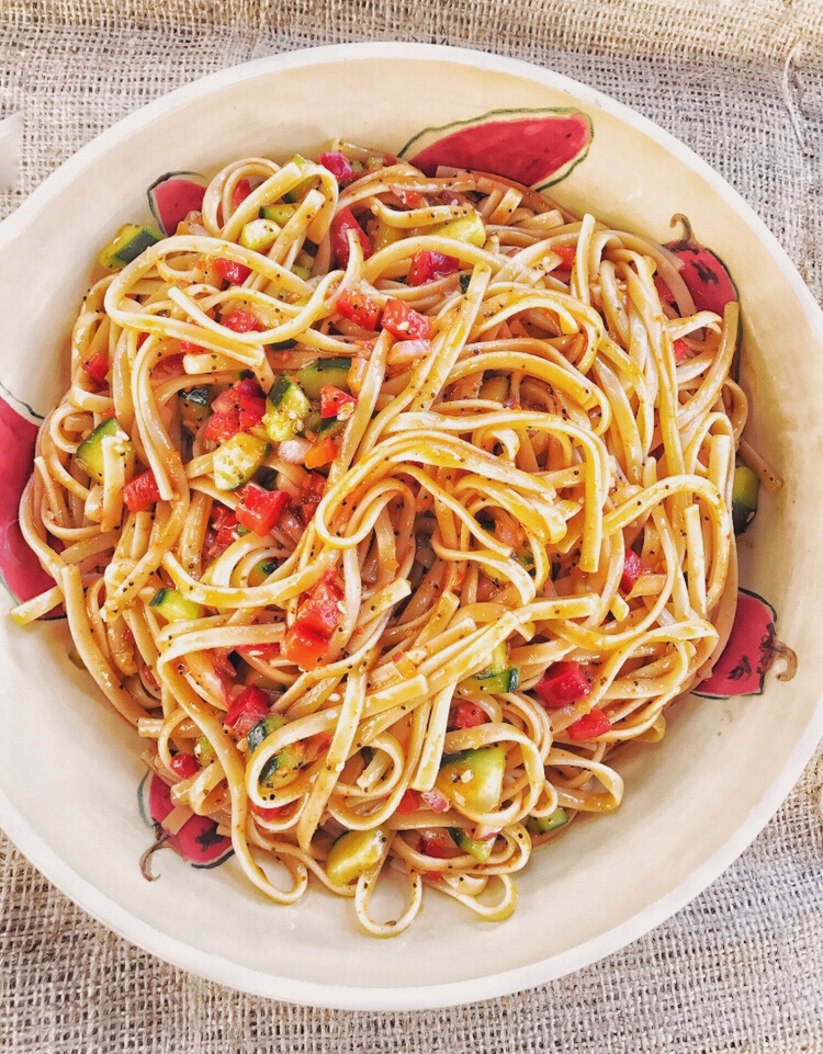 Linguine salad with diced vegetables in a white bowl with a red pepper design.