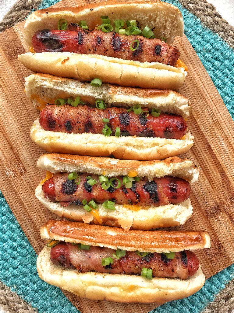 Four bacon wrapped hot dogs topped with chopped green onion.