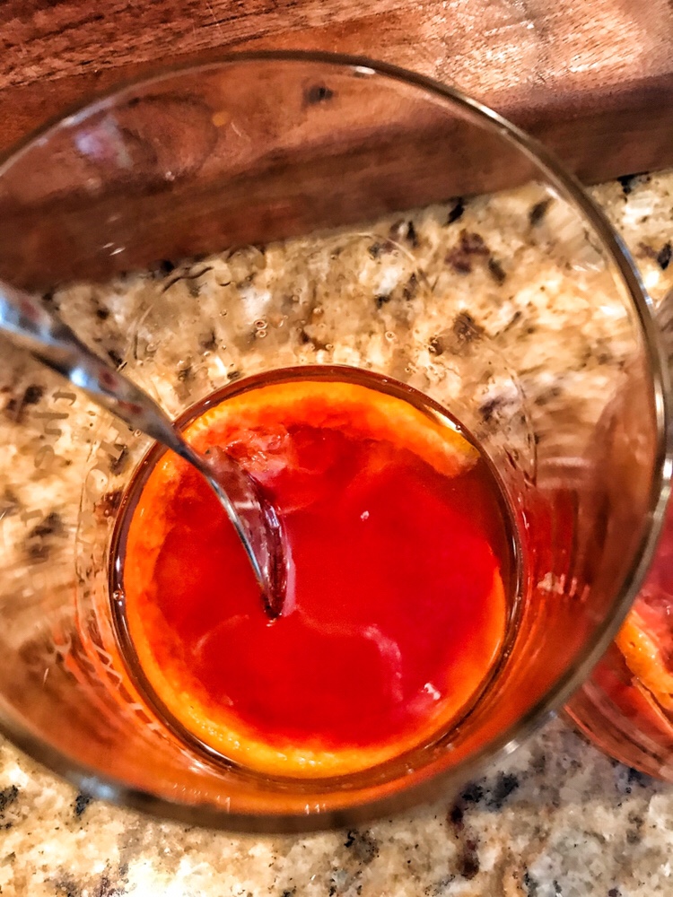 A spoon in a glass of brandy with muddled orange, cherry, and sugar.