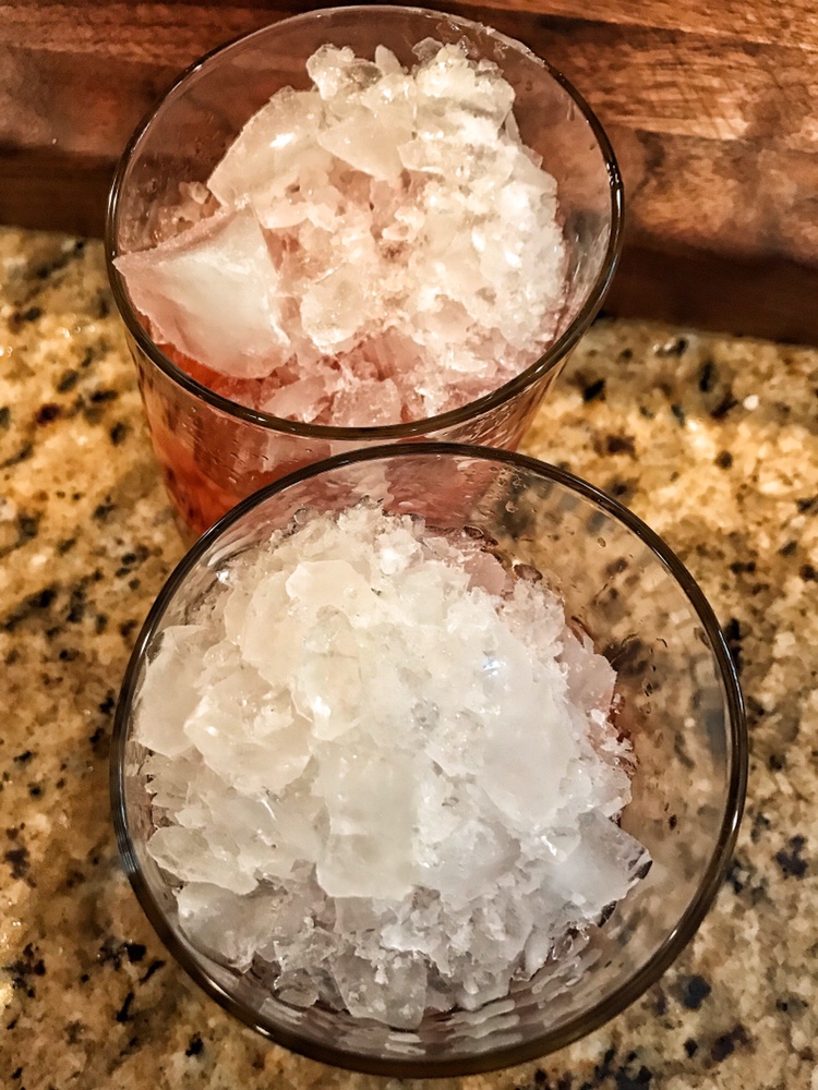 Two glasses full of crushed ice that covers the rest of their contents.