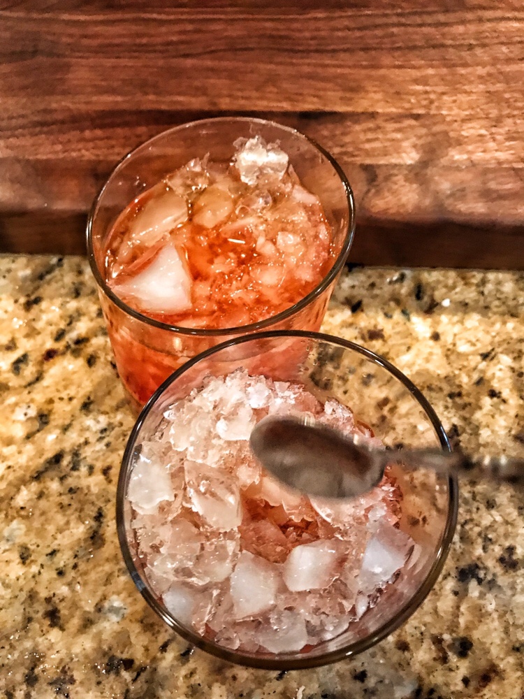Two glasses, one nearly filled with red liquid and the other partially filled with a spoon above it.