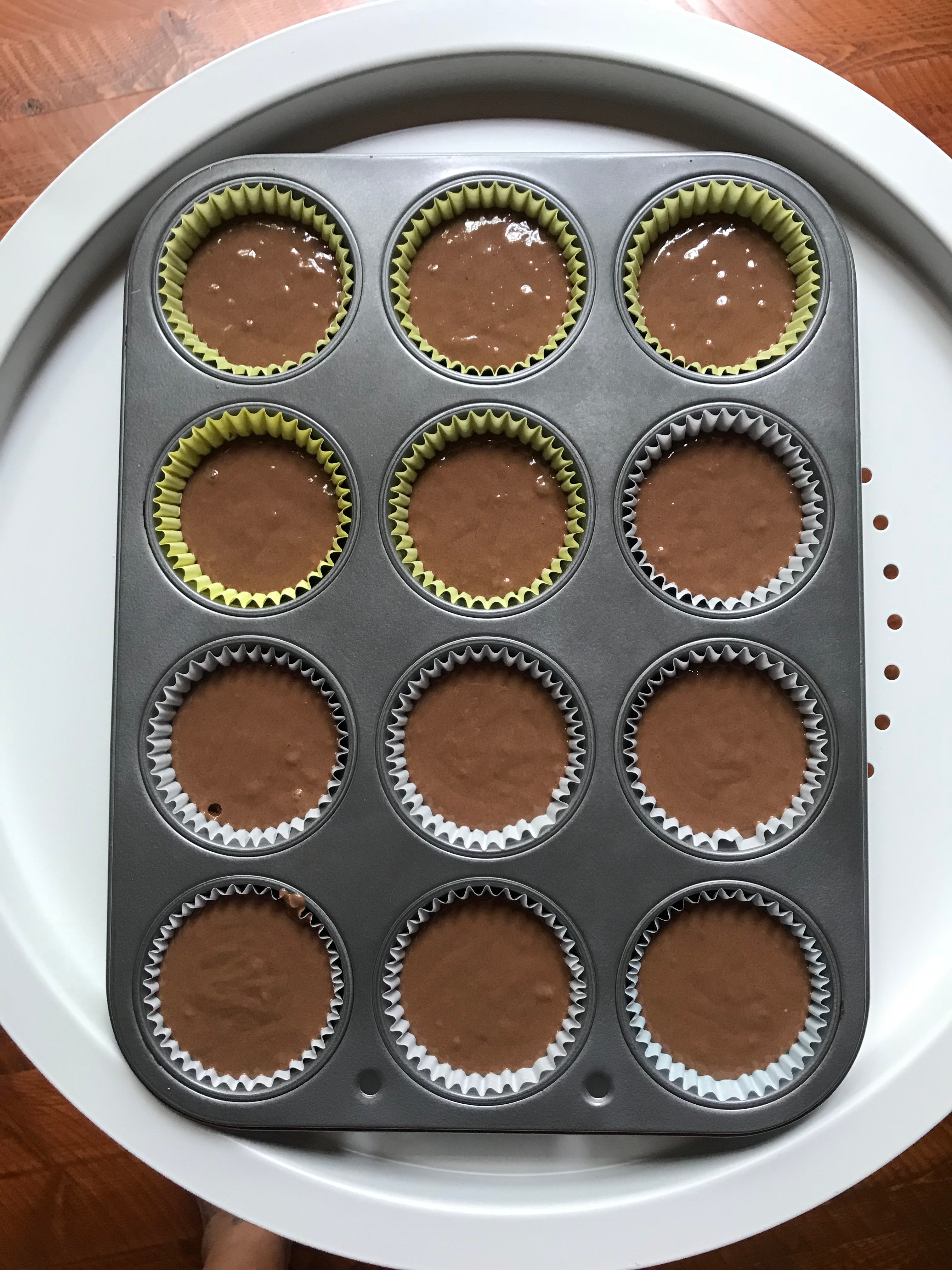 A cupcake tin filled with chocolate cake batter in liners.
