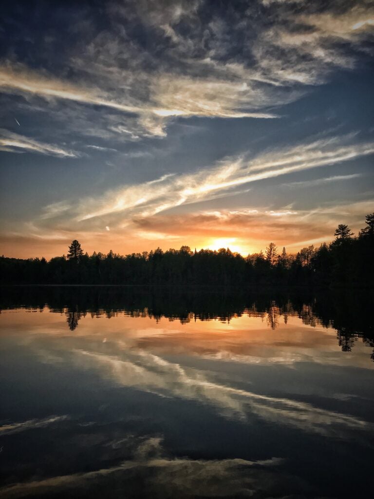 A sunset over a lake with trees in the background.