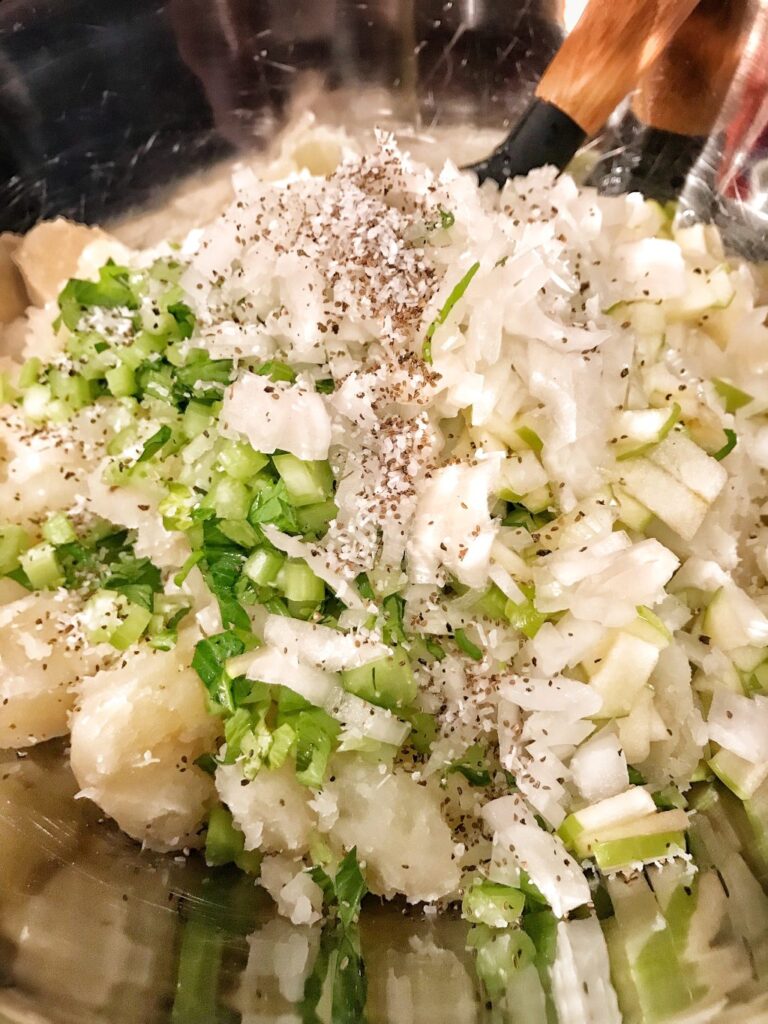 The chopped potatoes with the other ingredients for the salad on top in a metal bowl.