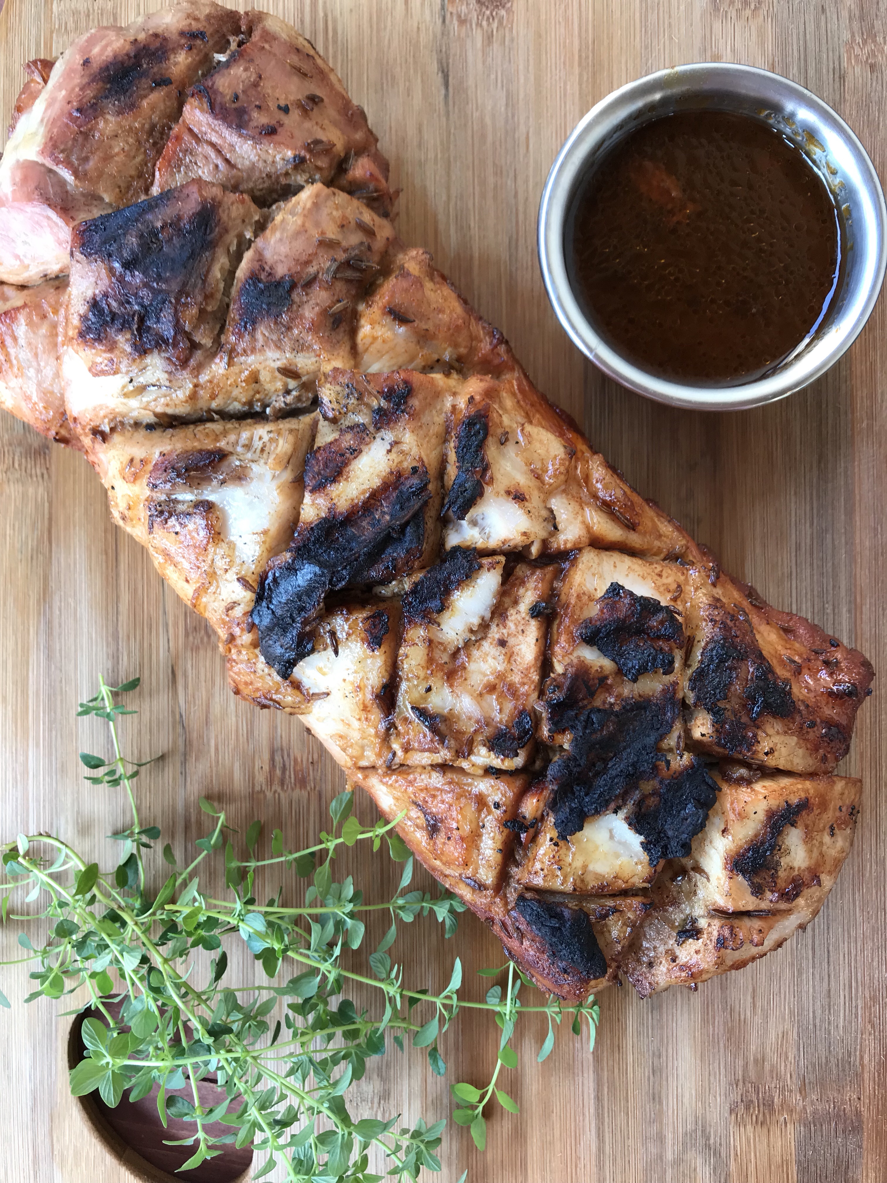 Roast pork tenderloin on a wooden cutting board with a cup of marinade.