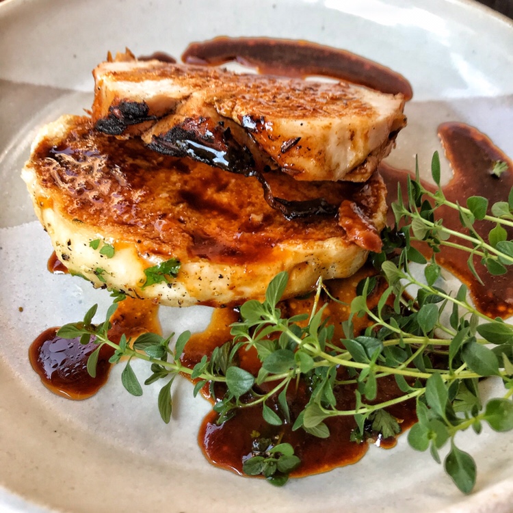 A slice of roast pork on a bread dumpling with marinade on a plate.
