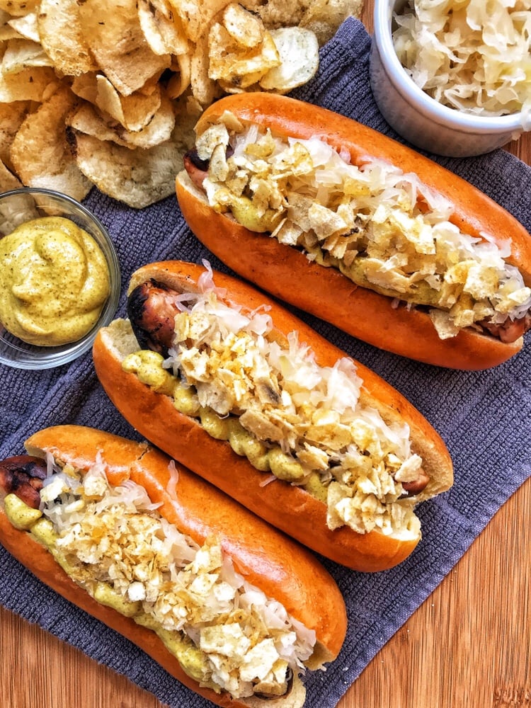 Three hot dogs with mustard, kraut, and crushed chips on top.
