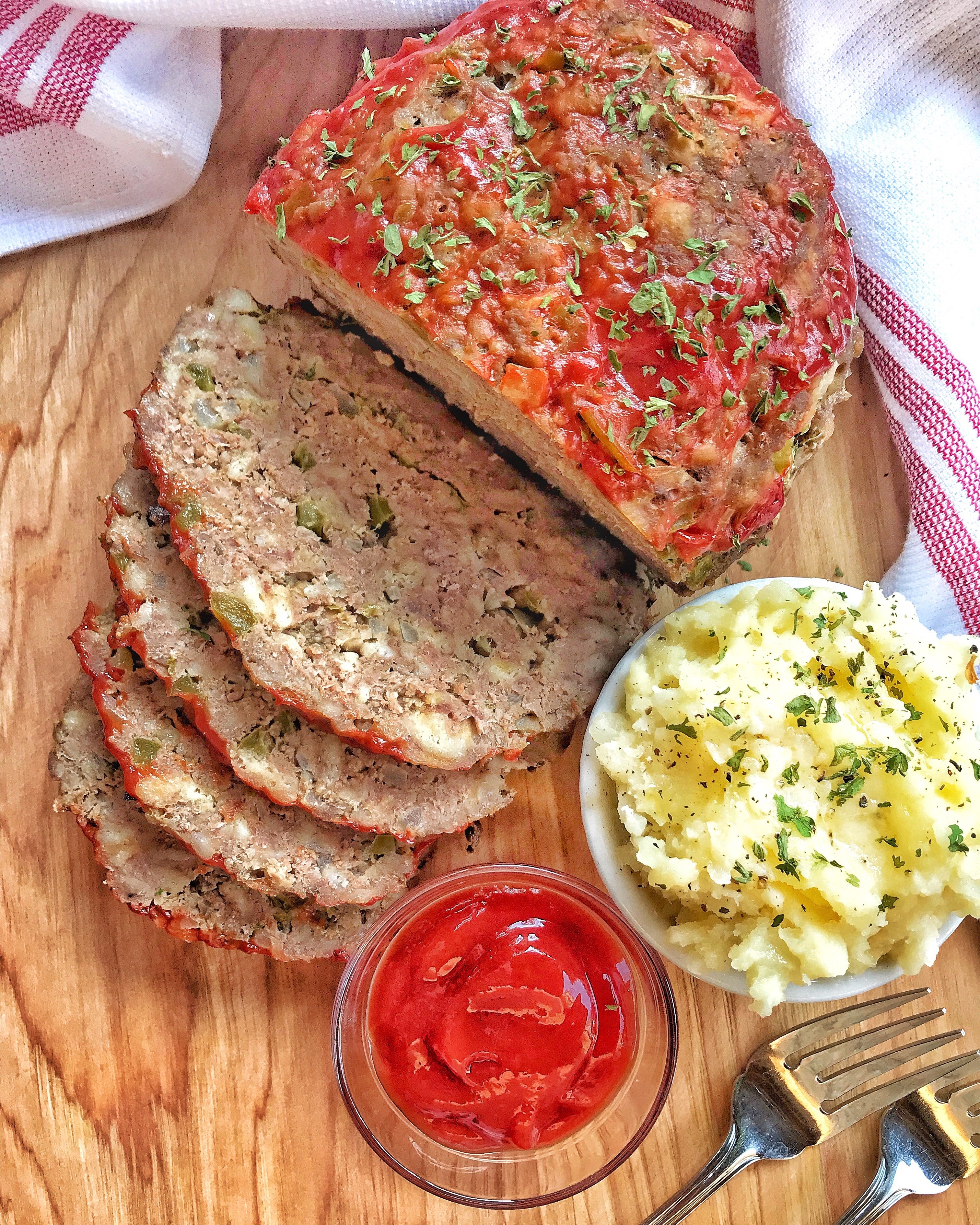 Sliced meatloaf next to mashed potatoes and ketchup.