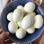Peeled, hard boiled eggs in a blue bowl.