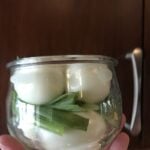 Peeled, hard boiled eggs in a jar with green onion.