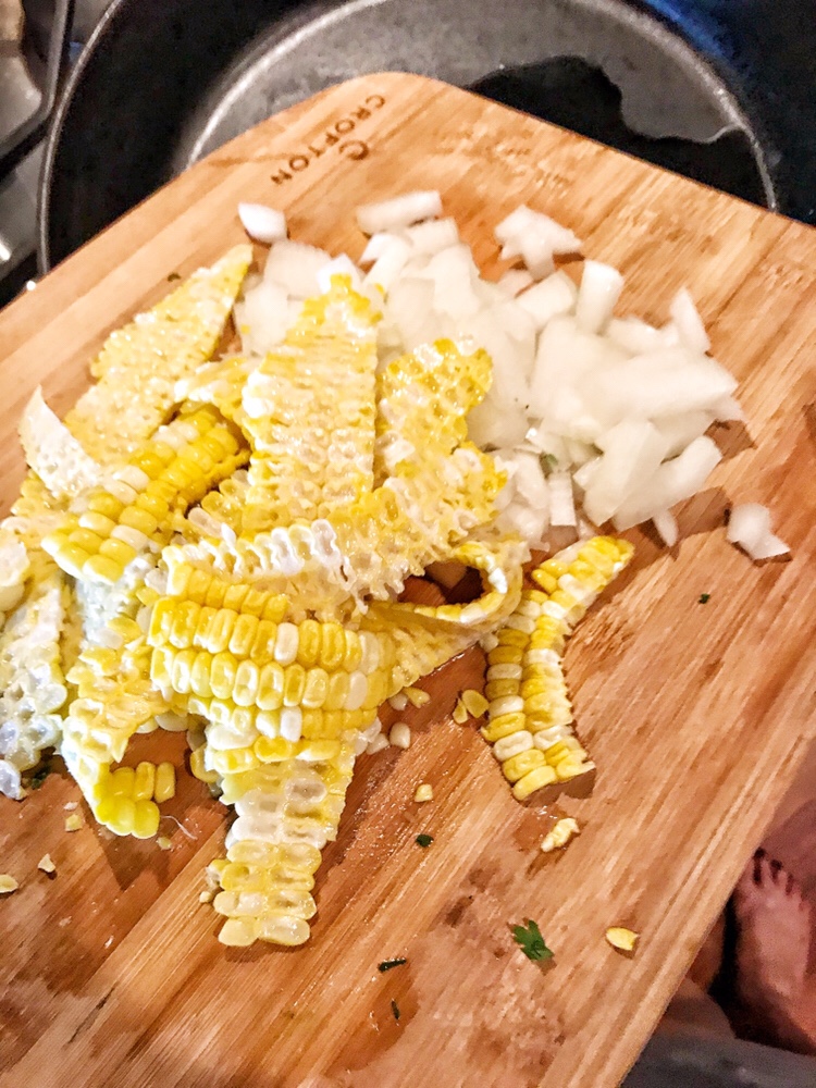 Corn cut from the cob and diced onion on a cutting board.