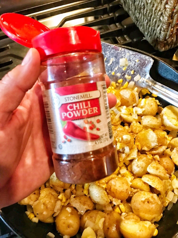 Chili powder held over the potatoes, corn, and onions in a pan.