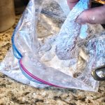 A chicken tender being removed from a plastic bag.