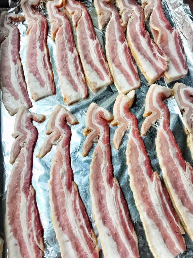 Raw bacon laid out on a baking sheet