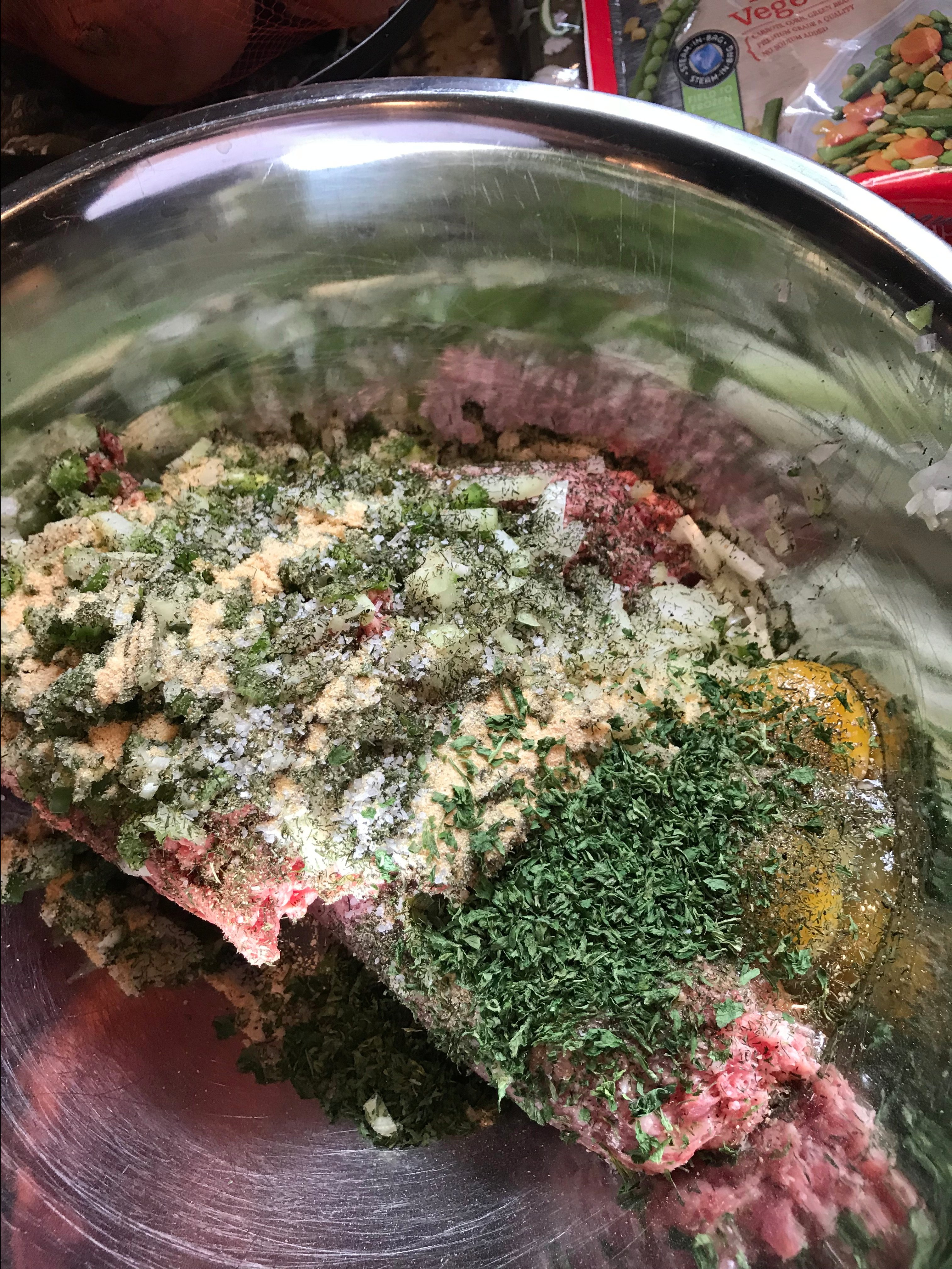 Ground meat, seasonings, and eggs in a metal bowl 