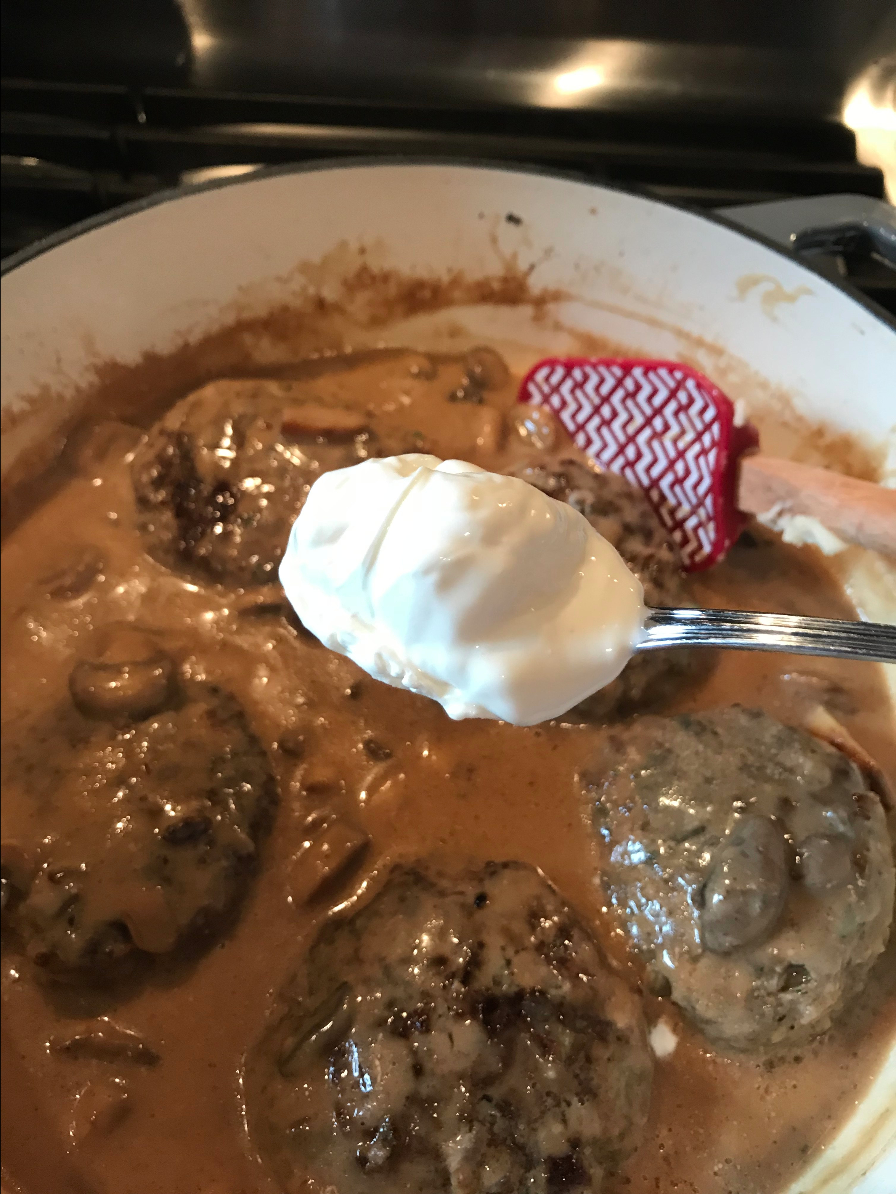 A spoon of sour cream about to be put in the cooking burgers