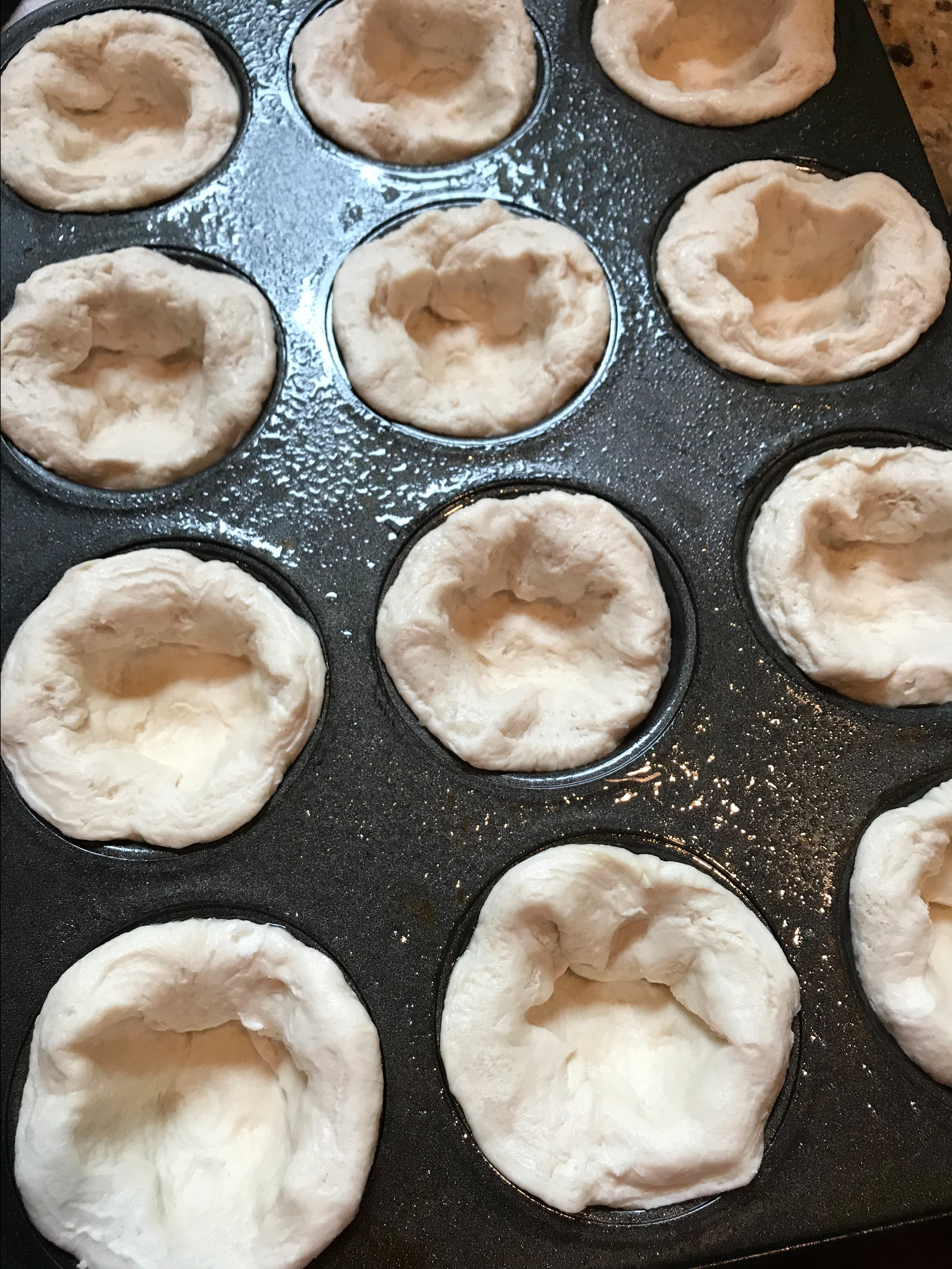 Biscuit dough pressed into the cups of a muffin tray