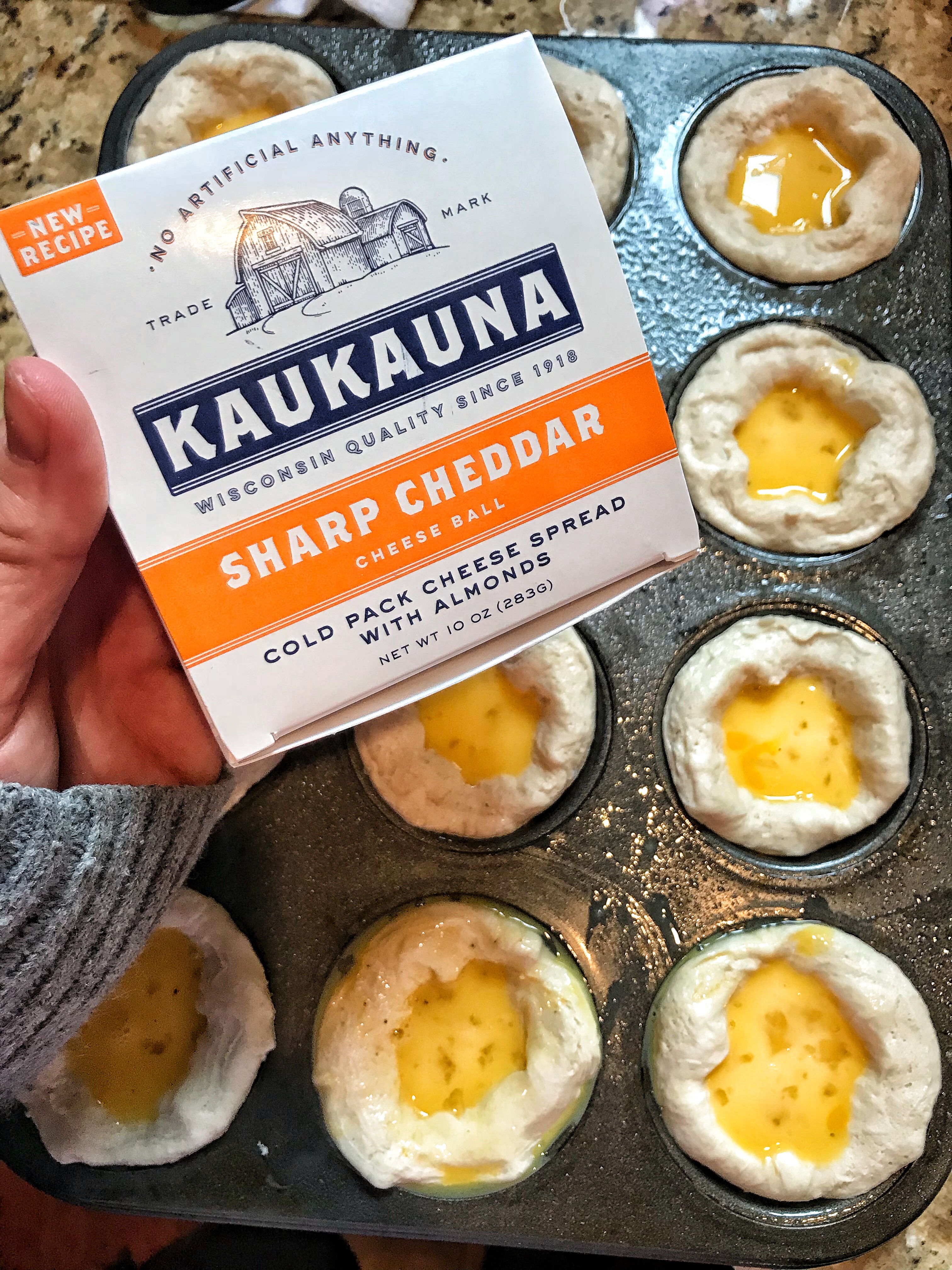 A package of Kaukauna sharp cheddar held over the biscuits before they are cooked