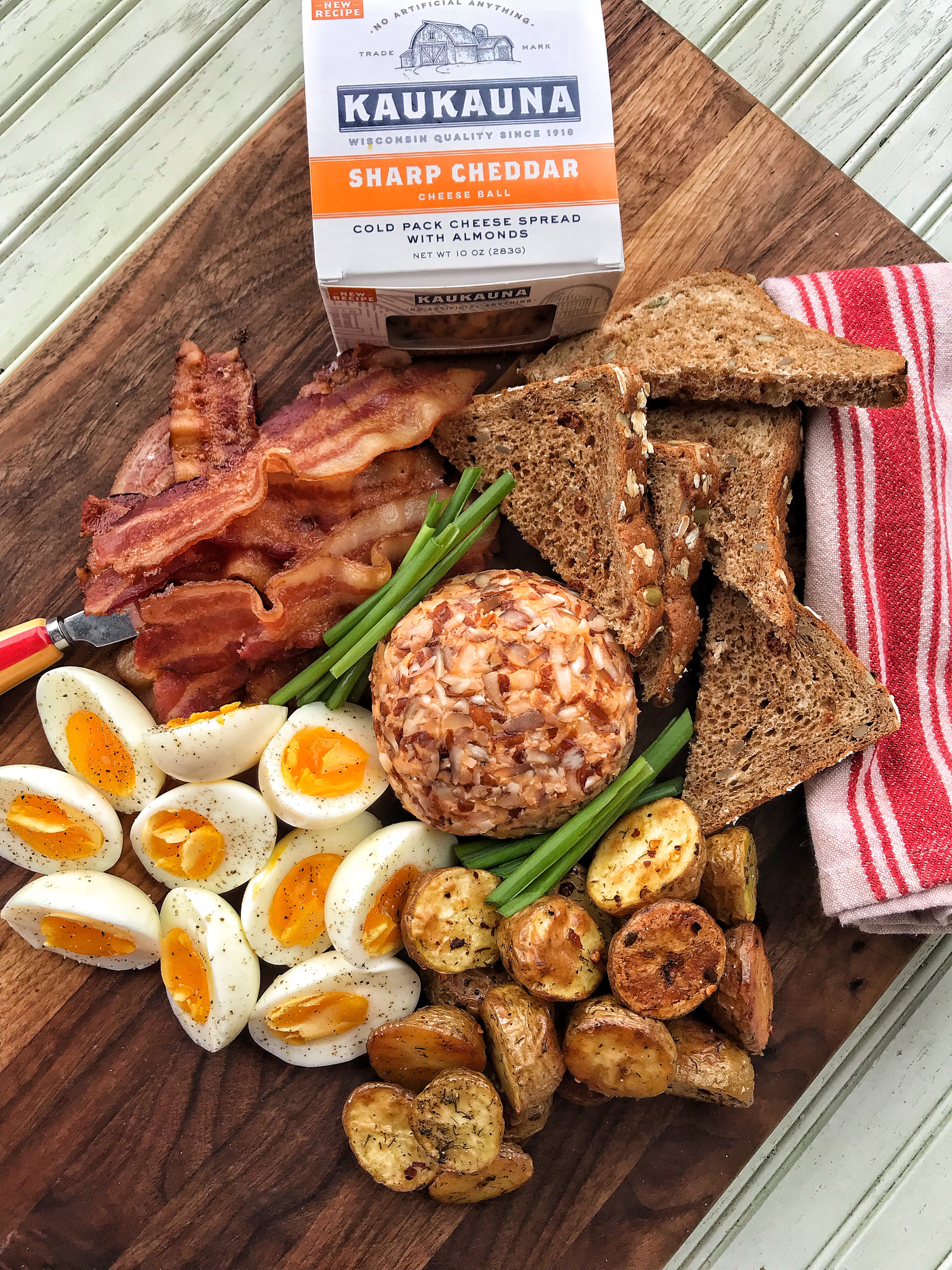 A breakfast board with toast, bacon, eggs, potatoes, and a Kaukauna cheese ball